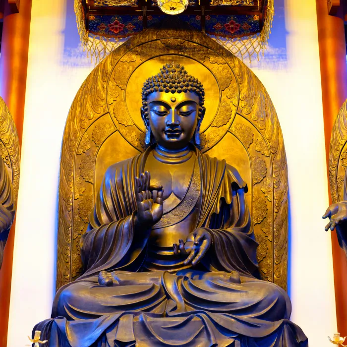 A majestic golden bronze statue of Gautama Buddha seated in meditation inside a temple shrine with warm overhead lighting. | PrintPosters.in