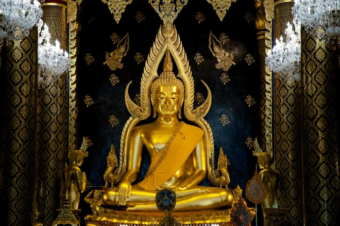 A majestic golden statue of Phra Buddha Chinnarat seated in meditation against a dark, ornate background with chandeliers. | PrintPosters.in