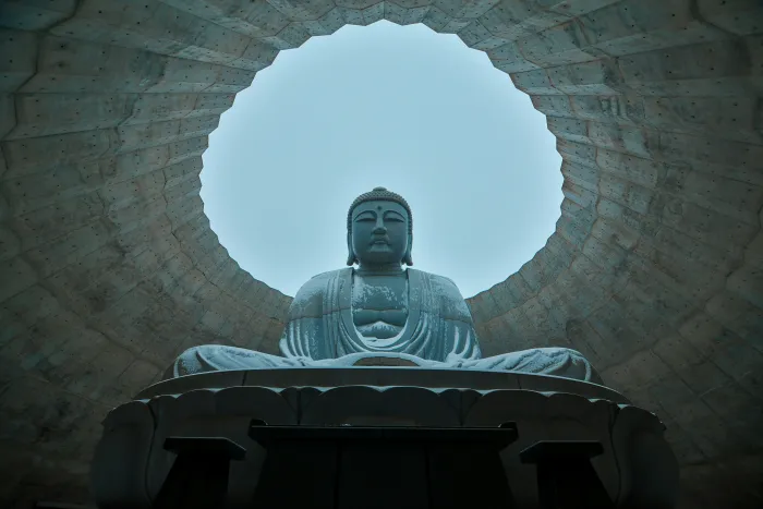 A low-angle photograph of a giant stone Lord Buddha statue framed by a circular concrete opening against a clear sky. | PrintPosters.in