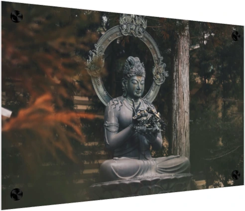 A dark bronze statue of a seated Buddha holding a flower, surrounded by green forest trees. — acrylic preview | PrintPosters.in