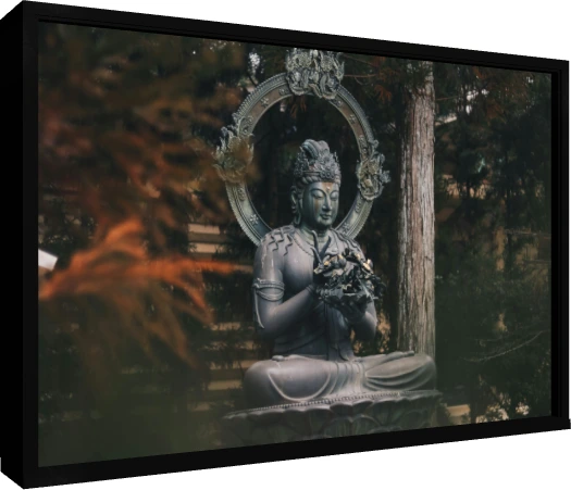 A dark bronze statue of a seated Buddha holding a flower, surrounded by green forest trees. — floater frame preview | PrintPosters.in