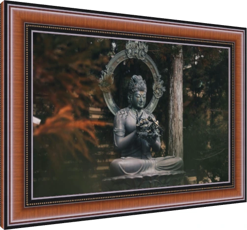A dark bronze statue of a seated Buddha holding a flower, surrounded by green forest trees. — photo frame preview | PrintPosters.in