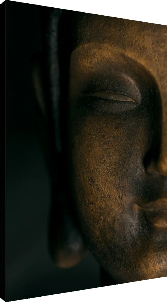 A close-up photograph of a dark bronze Lord Buddha face statue, illuminated from one side with deep shadows. | PrintPosters.in